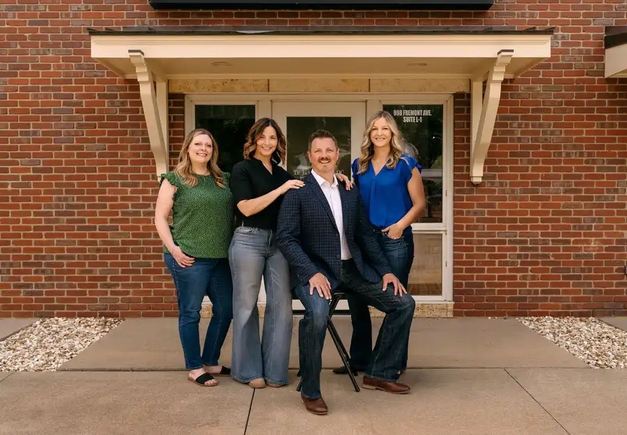 Team of four staff members posing outside a brick office building entrance